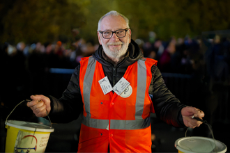 Smiling man with a beard wearing a high viz jacket, holding two collection buckets at the Somerset Carnivals