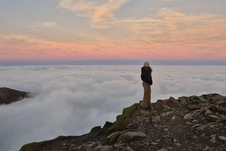 Girl standing at the top of Snowdon looking out above the clouds at sunrise