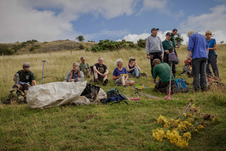 A group of people sat in a field, with tools