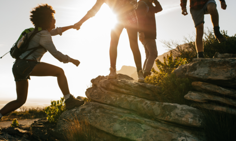 Woman helping her friend to climb up onto a rock