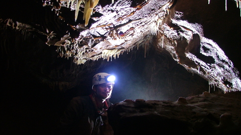 man with head torch deep underground beneath stalactites