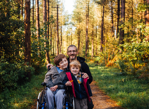 Two boys, one a wheelchair user, and their dad on a woodland path