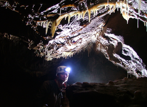 man with head torch deep underground beneath stalactites