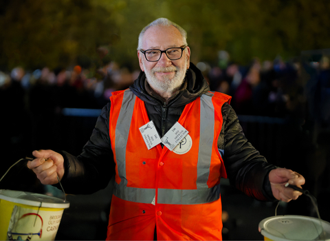 Smiling man with a beard wearing a high viz jacket, holding two collection buckets at the Somerset Carnivals