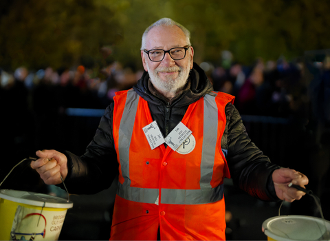 Smiling man with a beard wearing a high viz jacket, holding two collection buckets at the Somerset Carnivals